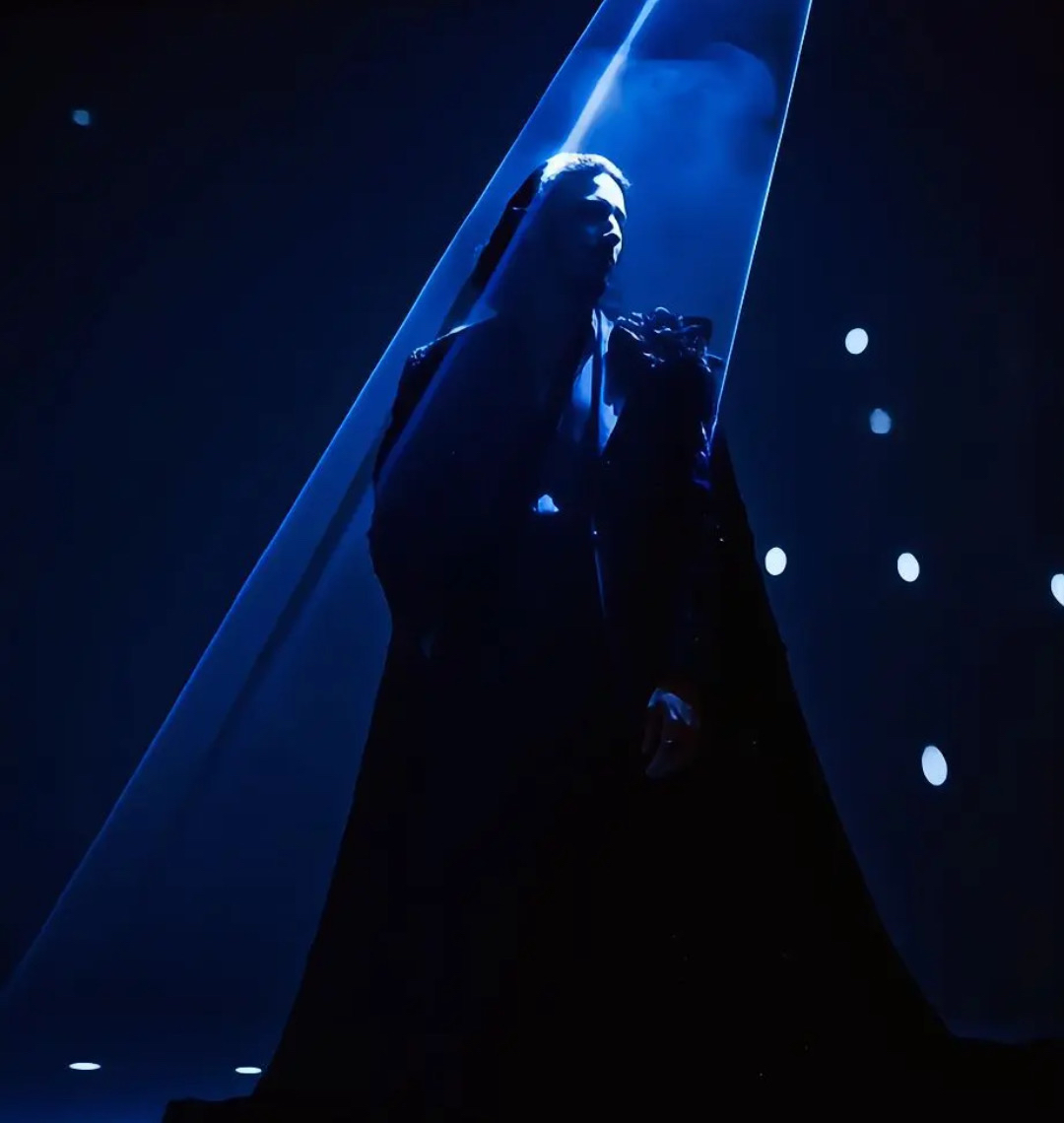 MEHDIY in a dark outfit beneath a vivid blue spotlight